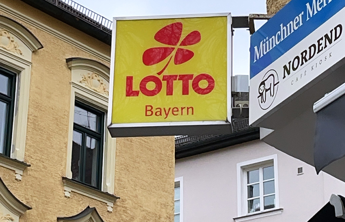 Ein Leuchtschild von LOTTO Bayern an der Hauswand über einer Annahmestelle