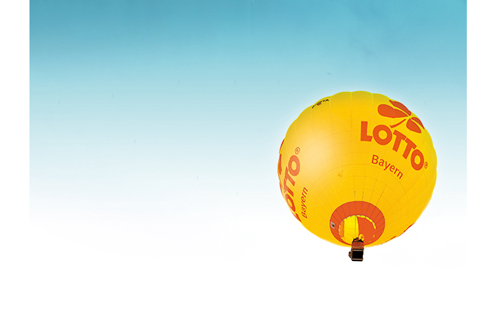Der LOTTO Bayern Heißluftballon schwebt vor dem blauen Himmel