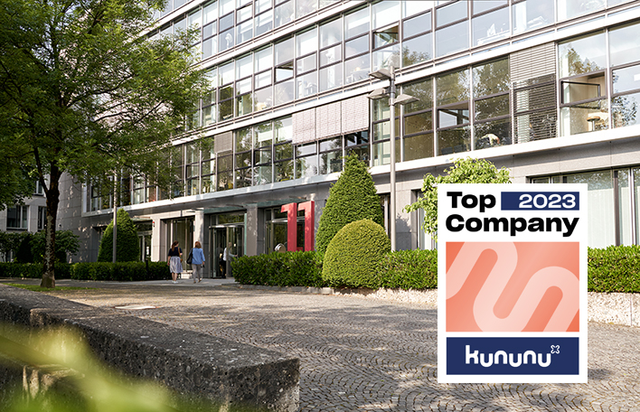 Eingangsbereich der Münchner Unternehmenszentrale, im Bild integriert das Logo der Auszeichnung "Top Company 2023" durch kununu.com